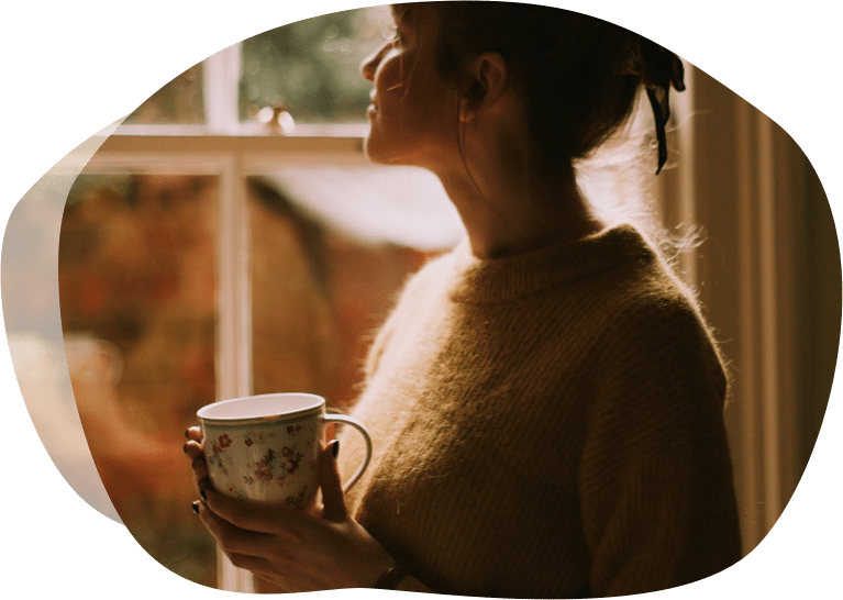 Dame som ser ut av vinduet mens hun drikker en god varm kopp kaffe.